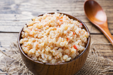 Boiled bulgur with tomatoes in a wooden bowl.