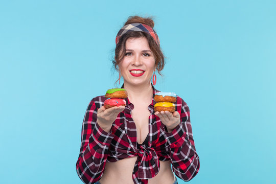 Positive young pin-up girl model holding in hands multicolored donuts posing on a blue background. Cooking concept for desserts and sweets.