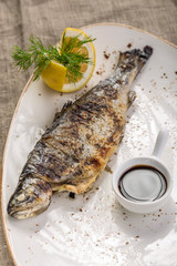 Grilled whole trout with lemon and soy sauce on white plate on tablecloth