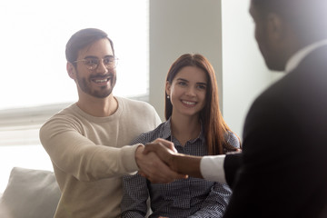 Excited millennial husband shaking hands with african american male broker.