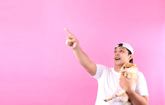 Wow, it's unbelievable. Shocked asia man opening mouth and dog  pomeranian pointing aside at copy space