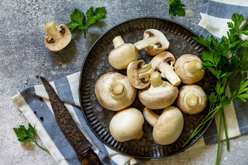 Champignons. Fresh white mushrooms in bowl on stone background. Top view of a flat lay.