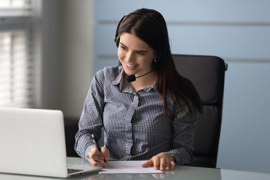 Smiling businesswoman watching educational webinar, writing down notes.