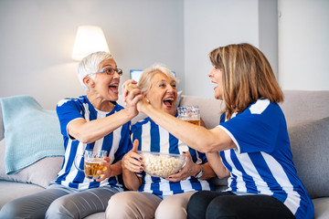 Elderly Woman Fans Emotionally Watching Soccer on Tv. Senior women watching football on TV. Cheerful fans in Sports Jersey. Female friends watching football game.