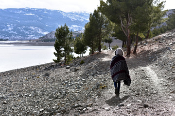 Young woman in wellies, hat & coat, walking on road with snow in winter, Salda Lake, Turkey