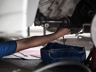 Professional car mechanic changing motor oil under car at the garage. Mechanic oil change service. 