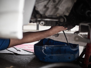 Professional car mechanic changing motor oil under car at the garage. Mechanic oil change service.    