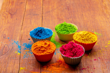 Fototapeta na wymiar Holi color powder. Organic Gulal colours in bowl for Holi festival, Hindu tradition festive. Blue, pink, magenta, orange, yellow holi dry paints on wood desk background