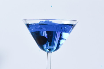 Cocktail with blue liquid in glass. Glass with blue water pouring with liquid with splashes and drops. Martini glass filling with alcohol with splashes on white background. Refreshing drink concept.