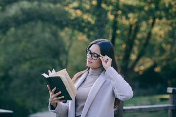 Fototapeta premium Smart brunette woman in eyeglasses reading book in park 