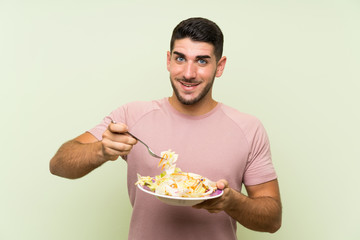 Young handsome man with salad over isolated green wall