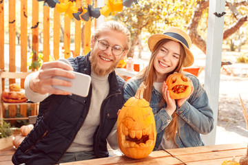 Halloween Preparaton Concept. Young couple sitting at table outdoors making jack-o'-lantern taking...