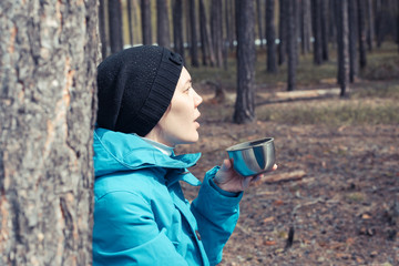 Mug of tea from thermos with tea in the hands of girl for warming in hiking trip in the forest.