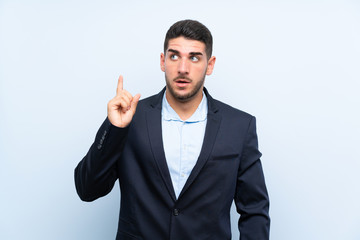 Handsome man over isolated blue background thinking an idea pointing the finger up