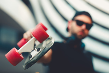 Young man holding a skateboard in his hand and posing in the city. Selective focus on skateboard. © djile