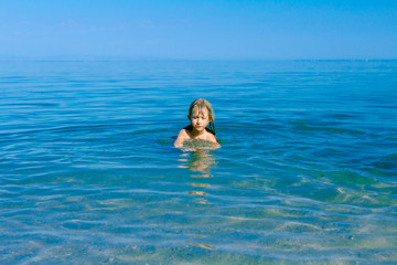 Excited child girl jumping with widespread hands in shallow sea water