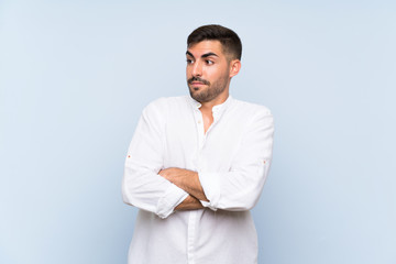 Handsome man with beard over isolated blue background making doubts gesture while lifting the...