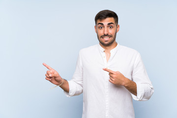 Handsome man with beard over isolated blue background frightened and pointing to the side