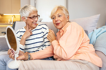 Senior women spending time together at home. Cheerful positive attractive senior lady friends looking at the mirror satisfied with nature beauty. Two cheerful senior women chatting at home.