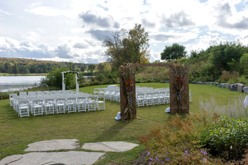 Place for wedding ceremony at the Lakeshore. Wedding arch decorated with flowers and white chairs on each side of archway outdoors