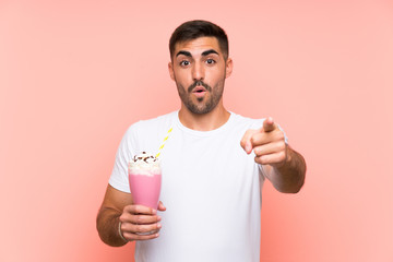 Young man with strawberry milkshake over isolated pink background surprised and pointing front
