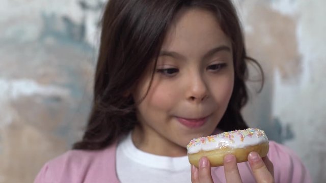 Little girl alone isolated on painted wall looking at donut foretasting