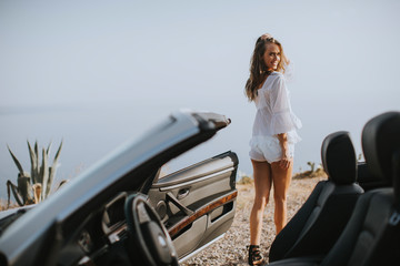 Pretty young woman by the white cabriolet car on the seaside