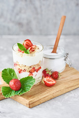 granola or yogurt with strawberry in glass, fresh berries and jar with sugar on a cutting board, top view