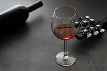 Guitar and high glass with red wine on a stone background.