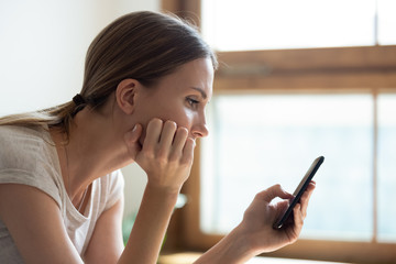 Pensive sad young woman holding smartphone waiting sms from boyfriend