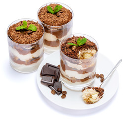Classic tiramisu dessert in a glass cup on the plate and pieces of chocolate on white background with clipping path