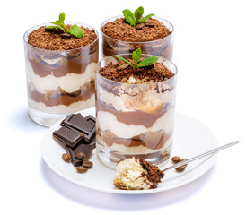 Classic tiramisu dessert in a glass cup on the plate and pieces of chocolate on white background with clipping path