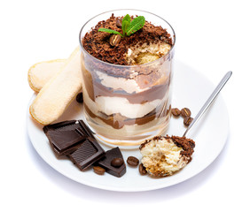 Classic tiramisu dessert in a glass cup on the plate and pieces of chocolate on white background with clipping path