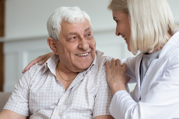 Middle-aged nurse hug elderly man patient sitting on couch