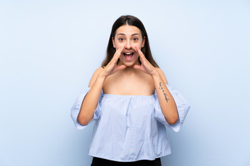 Young brunette woman over isolated blue background shouting with mouth wide open