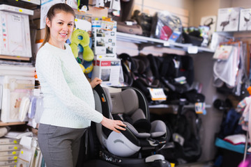 Pregnant smiling woman is choosing baby seat for car