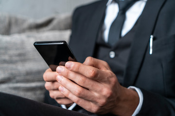 Close up of businessman hands using smartphone in blurred armchair. Concept of online communication and social media