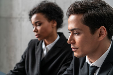 Portrait of young business people. Serious Caucasian businessman and African American woman in background. Focus on businessman. Teamwork concept
