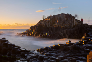 Long exposure sunset at Giant Causeway with shadows of moving people standing on rocks creating a ghost effect