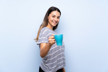 Young brunette woman over isolated blue background holding hot cup of coffee