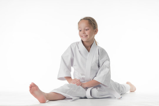 little karate girl in a white kimono and a  belt sits for a workout in sports twine