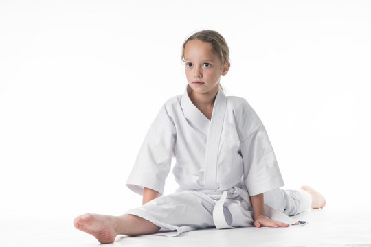 little karate girl in a white kimono and a  belt sits for a workout in sports twine