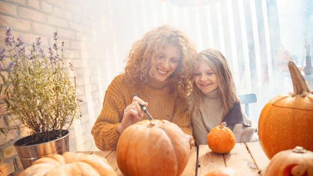 Young adult mother carving pumpkin with her little daughter