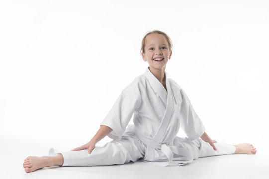 little karate girl in a white kimono and a  belt sits for a workout in sports twine