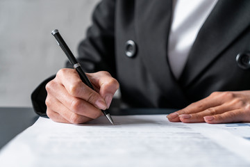 Close up of young woman hands writing or signing contract. Blurred background. Concept of management and CEO work