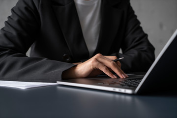 Unrecognizable young woman in business suit using laptop touchpad and taking notes at office table. Concept of business and education