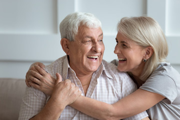 Elderly hoary couple embracing sitting on couch indoors