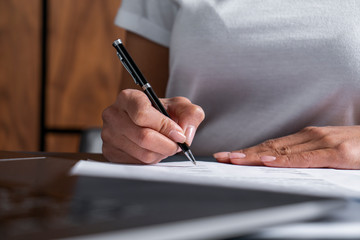 Close up of unrecognizable woman hands signing document at office table with laptop. Concept of paperwork and management.