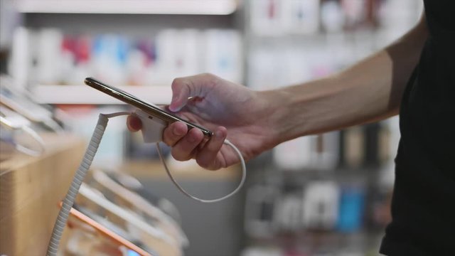 Young unrecognizable man chooses a smartphone in an electronics store, close-up. He takes smart phone from counter and trying using it.