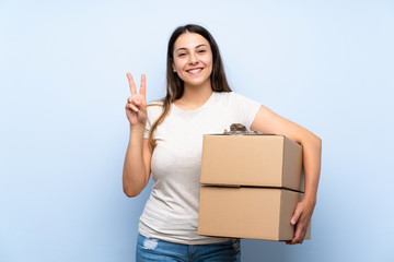 Young delivery woman over blue brick wall smiling and showing victory sign